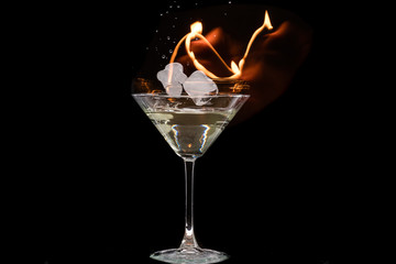 glass of martini with olives and ice on a black background and fire