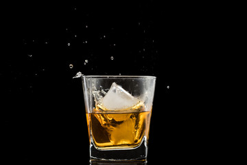 glass with whiskey and falling ice, splashes and drops