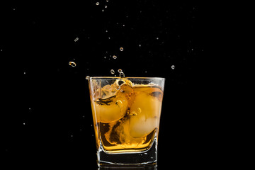 glass with whiskey and falling ice, splashes and drops