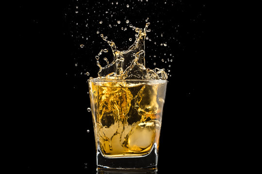 glass with whiskey and falling ice, splashes and drops