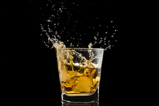 glass with whiskey and falling ice, splashes and drops