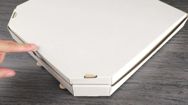 A man's hand closes a paper box in which there is a fragrant freshly baked pizza. Delivery of pizza in a box.