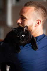 Bearded vet caresses black cat and smiles. Caring for pets.