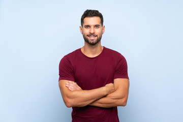 Handsome man over isolated blue background keeping the arms crossed in frontal position