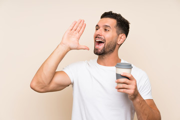 Young man with beard holding a take away coffee over isolated blue background shouting with mouth wide open