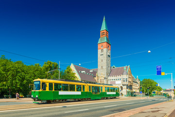 View of a city tram in Helsinki and the old historical building of The National Museum of Finland with clear blue sky in the background