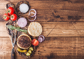 Fresh grilled minced pepper beef burger on vintage chopping board with buns onion and tomatoes on wooden background. Top view . Space for text