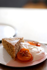 Slice of homemade sponge cake served on a table with whipped cream, cooked apricots and walnuts. Selective focus.