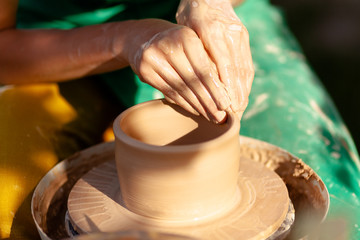 Hand craft making pottery on wheel. Female hands mold ceramic plate from clay (pot).