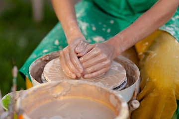 Hand craft making pottery on wheel. Female hands mold ceramic plate from clay (pot).