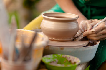 Hand craft making pottery on wheel. Female hands mold ceramic plate from clay (pot).