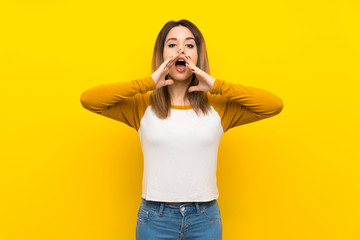 Pretty young woman over isolated yellow wall shouting and announcing something