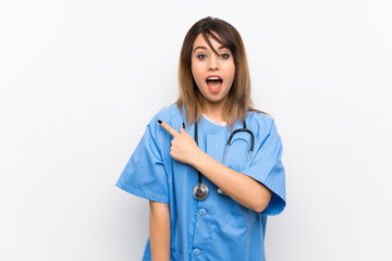 Young nurse woman over white wall surprised and pointing side