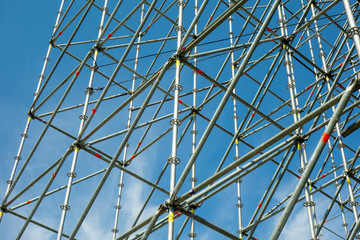 Naklejka premium Metal pipe frame structure on blue sky background. Industrial construction from tubes raises upwards. Building process and joining elements view. Straight and inclined lines backdrop