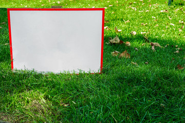 Warning table with copy space in green grass. Mock up for park or garden signs, blank to add text or image regarding nature, ecology or other concepts. Information display among foliage