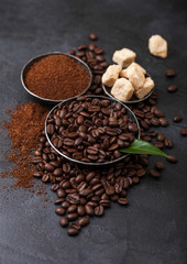 Fresh raw organic coffee beans with ground powder and cane sugar cubes with coffee trea leaf on black background.