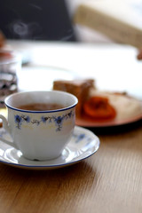 Cup of coffee and slice of homemade sponge cake served on a table with whipped cream, cooked apricots and walnuts. Selective focus.