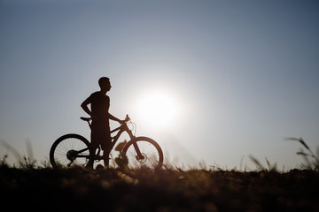 The silhouette of a bicycle and rider against the blue sky at sunset