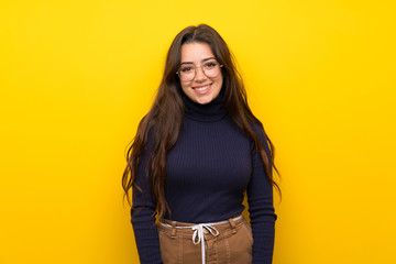 Teenager girl over isolated yellow wall with glasses and happy