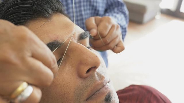 Eyebrow hair epilation, plucking. Beautician makes threading hair removal procedure. Threading, epilation technique in beauty salon. Ancient method of eyebrows hair removing in close-up.