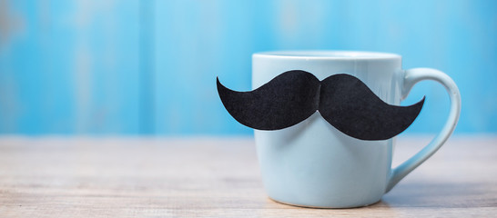 Blue coffee cup with Black mustache on wood table background in the morning. Father, International men day, Prostate Cancer Awareness and World cancer day concept