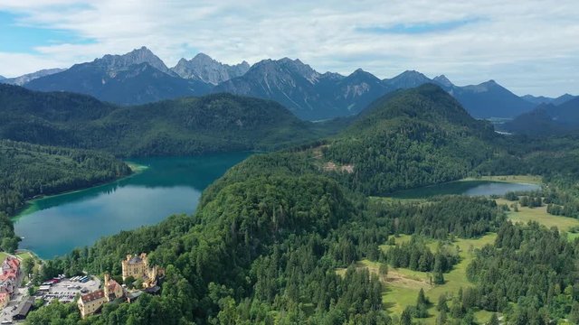 Aerial view of Hohenschwangau Castle in summer, picturesque palace in Bavarian Alps mountains, lush green hills and blue sky, lake Alpsee - landscape panorama of Bavaria from above, Germany, Europe