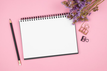 Top view of notebook and purple flower on pink background