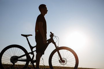 The silhouette of a bicycle and rider against the blue sky at sunset