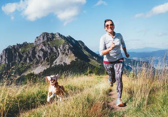 Happy smiling female jogging by the mounting range path with her beagle dog. Canicross running...