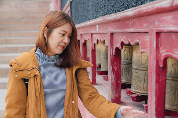 Beautiful young asian woman in yellow jacket rotating praying wheels for religious reason at...