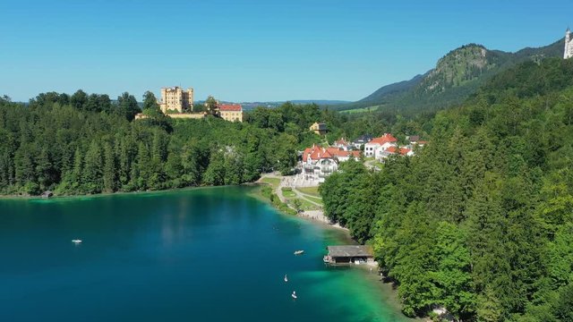 Aerial view of Hohenschwangau Castle in summer, picturesque palace in Bavarian Alps mountains, lush green hills and blue sky, lake Alpsee - landscape panorama of Bavaria from above, Germany, Europe