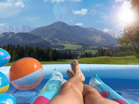 Mann liegt mit Wasserball und Luftmatratze im Pool mit Blick auf die Berge