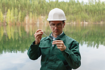 industrial ecologist takes a sample of water from lake at the site of a flooded quarry