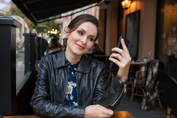 A young girl taking a selfie on her cell phone  in the cafe in the summer terrace.