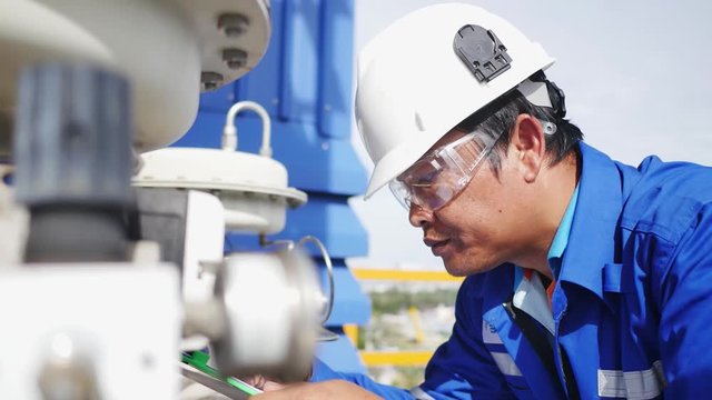 Close up of Engineer on site checking instrument equipment and record on paper clipboard , Oil and gas petroleum refinery plant working concept