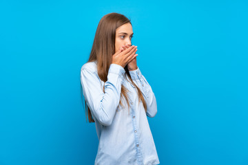 Young woman over isolated blue background covering mouth and looking to the side