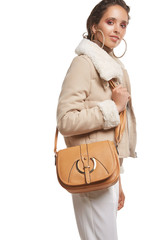 Medium full shot of a young chestnut European lady with a shoulder bag is wearing white casual trousers, a beige turtleneck and a short cream jacket with a fur trim. The bag is made of smooth sandy  © RedUmbrella&Donkey