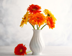 Beautiful bouquet of red and yellow flowers in white vase on wooden table, front view. Autumn still...