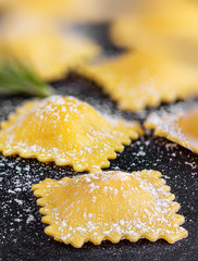 Raviolli with flour and herbs on black background, close up.  Italian Food