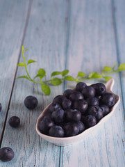 Blueberry with leaves in plate on wooden table.