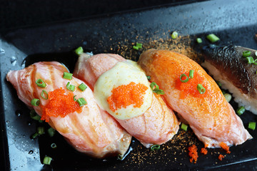 Top view colorful Salmon Sushi with tobiko eggs on top in black plate background. Japanese Foods concept. Dark tone.