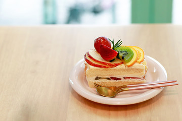Close Up Vanilla Cake with fruits on top, strawberry, kiwi, orange, apple and cherry, in the white plate on the wooden table background. Dessert concept.