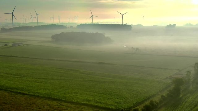 Large wind turbines turning slowly in the misty stillness of morning twilight.