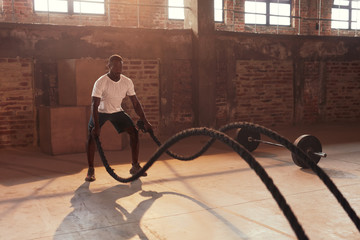 Fitness workout. Sport man doing battle rope exercise at gym