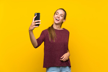 Young woman over isolated yellow background making a selfie