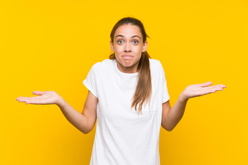 Young woman over isolated yellow background having doubts with confuse face expression