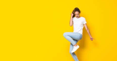 Fototapeta na wymiar Young woman jumping over isolated yellow wall