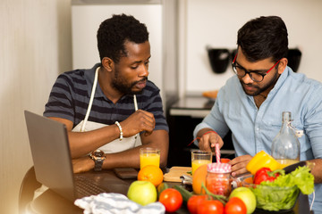 Two men using laptop in kitchen