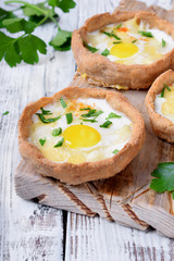 Baked rye tartlets with cheese and quail eggs on white wooden table