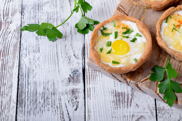 Baked rye tartlets with cheese and quail eggs on white wooden table